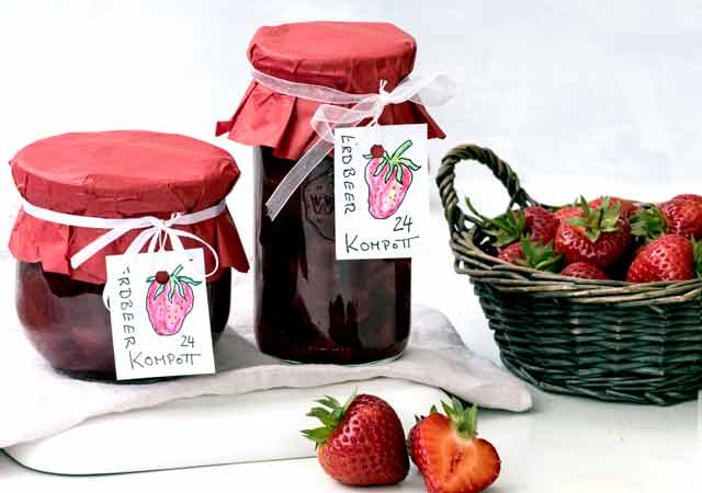 Ein Korb mit frischen Erdbeeren. Daneben zwei Gläser mit eingemachtem Erdbeerkompott.