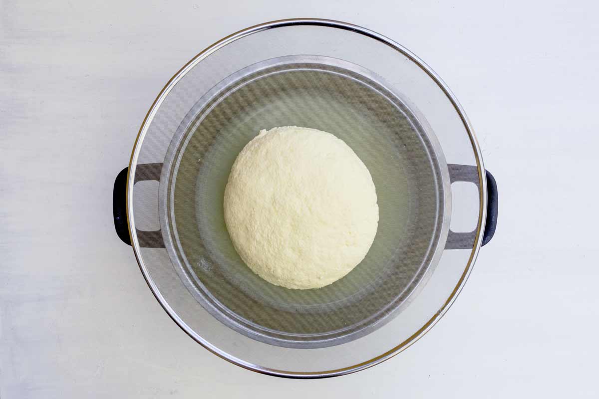 Ein Topf mit einem Sieb auf dem der gepresste Käsebruch zum abtropfen liegt