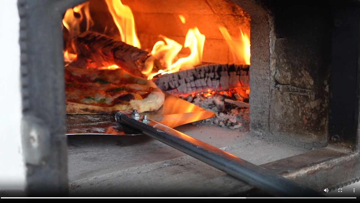 Eine neapolitanische Pizza wird im Holzofen abgeflämmt.
