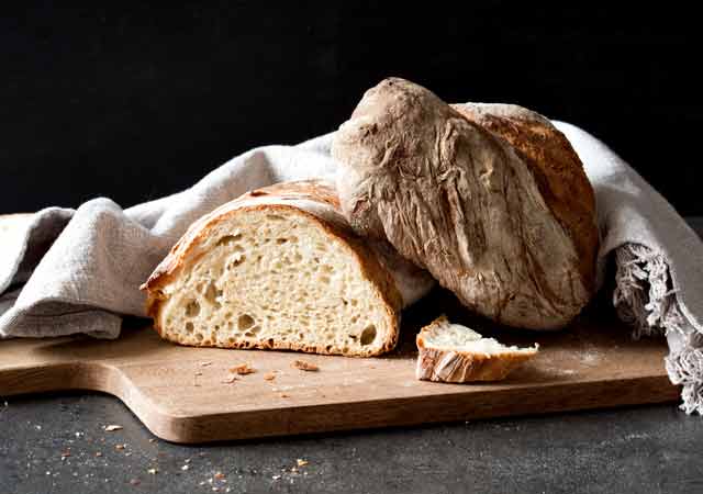 Frisch gebackenes Wurzelbaguette aus dem Holzofen. Geschnitten in zwei Teile und einer Scheibe Brot