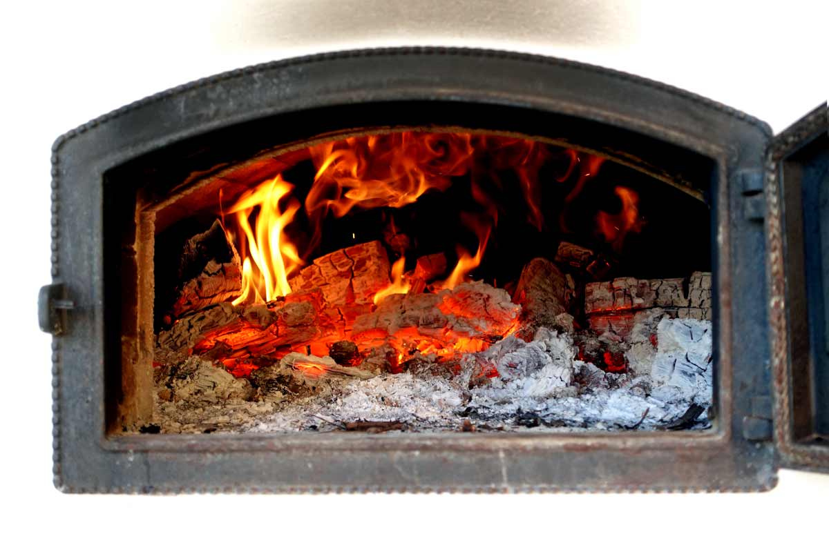 Blick in die offene Tür eines Holzbackofens. Das Holz ist dabeu zur Glut zu verbrennen. Es loder Feuer und es raucht.