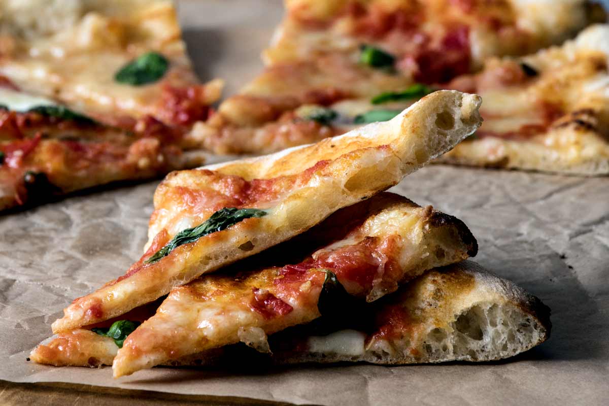 Drei übereinander gestapelte Pizzastücke einer frisch gebackenen neapolitanischen Pizza aus dem Holzofen