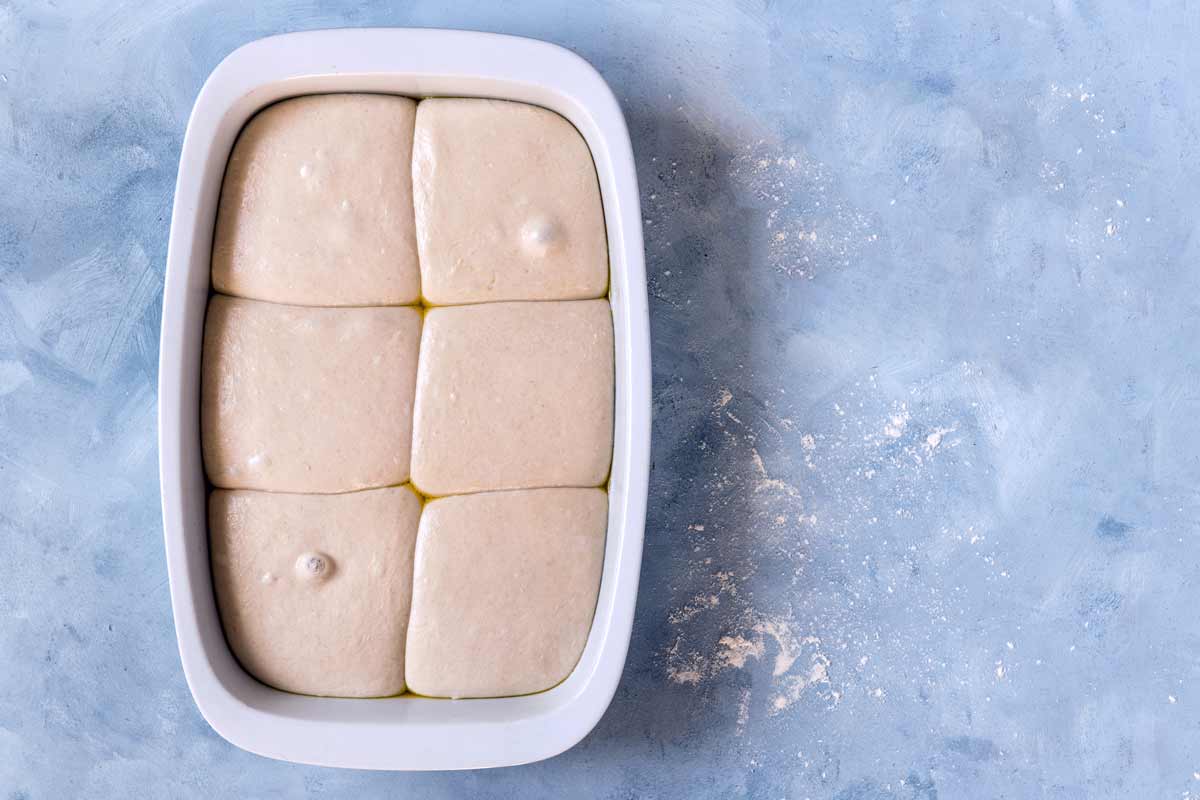 Sechs Pizzateiglinge in einer Form nach einer Ruhezeit 20 Stunden im Kühlschrank