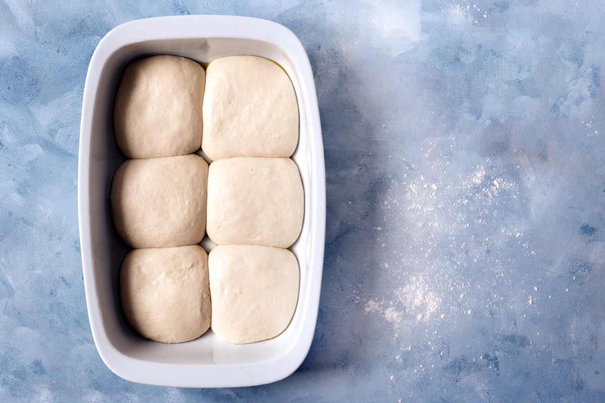 Sechs Pizzateiglinge in einer Form nach einer Ruhezeit von 30 Minuten