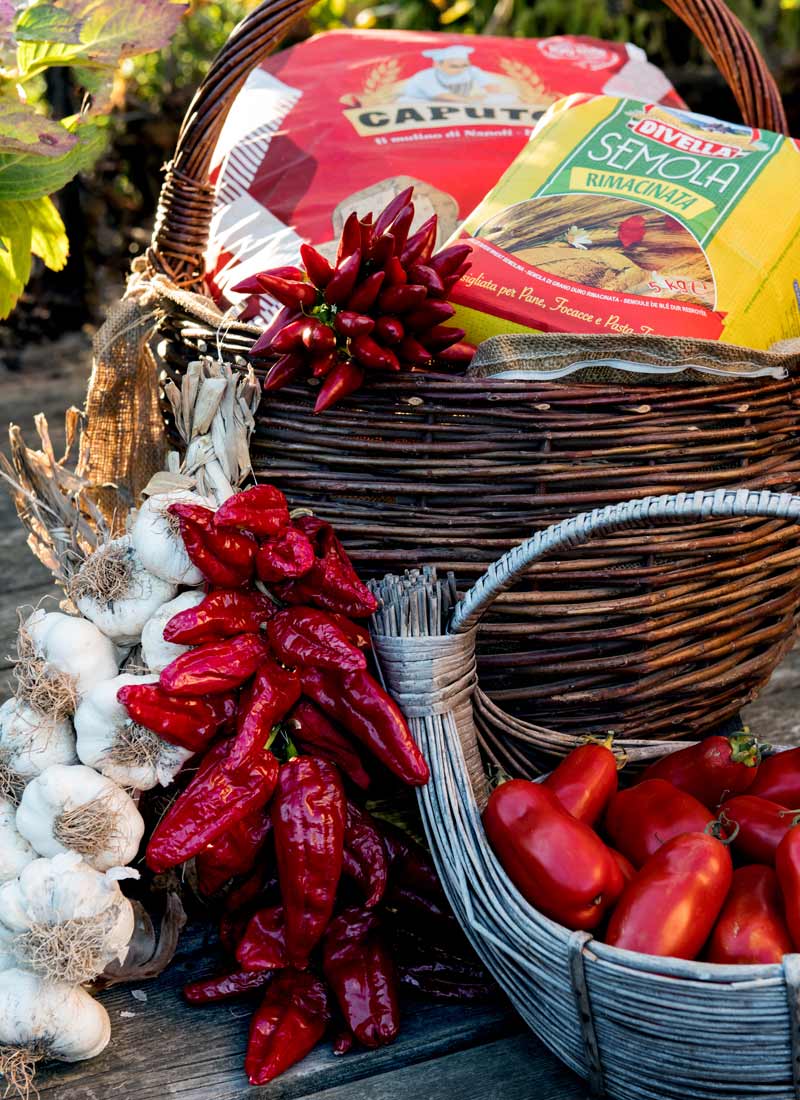 Originale Zutaten für eine authentische neapolitanische Zutaten arrangiert in einem Korb: Weizenmehl Typ 00, Semola Rimacinata , San Marzano Tomaten aus dem eigenen Garten, ein Zopf mit Knoblauch und frische Chillis