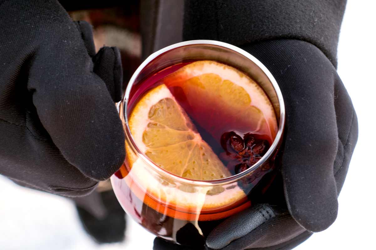 Hand mit schwarzem Handschuh hält dampfenden Glühwein-Becher