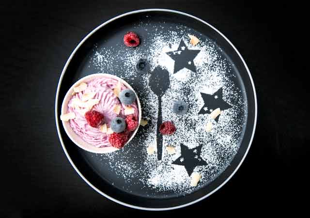 Sahnig, cremig und lockerer Frozen Skyr auf euinem schwarzen Teller, dekoriert mit gefrorenen Beeren