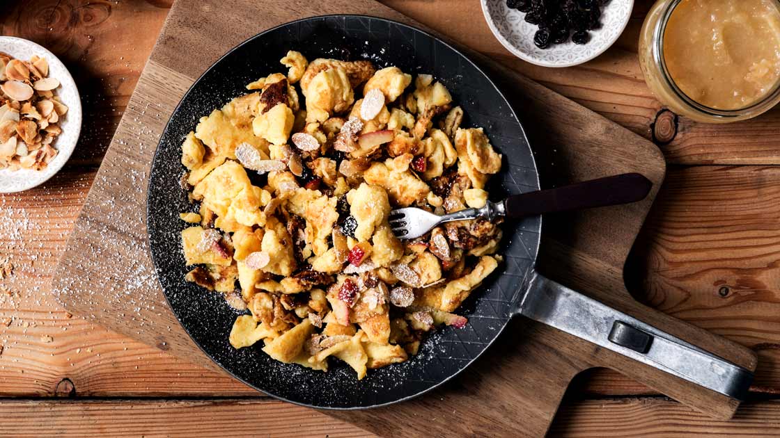 Eine Portion Kaiserschmarrn mit Äpfeln, Nüssen und Rosinen in einer Eisenpfanne