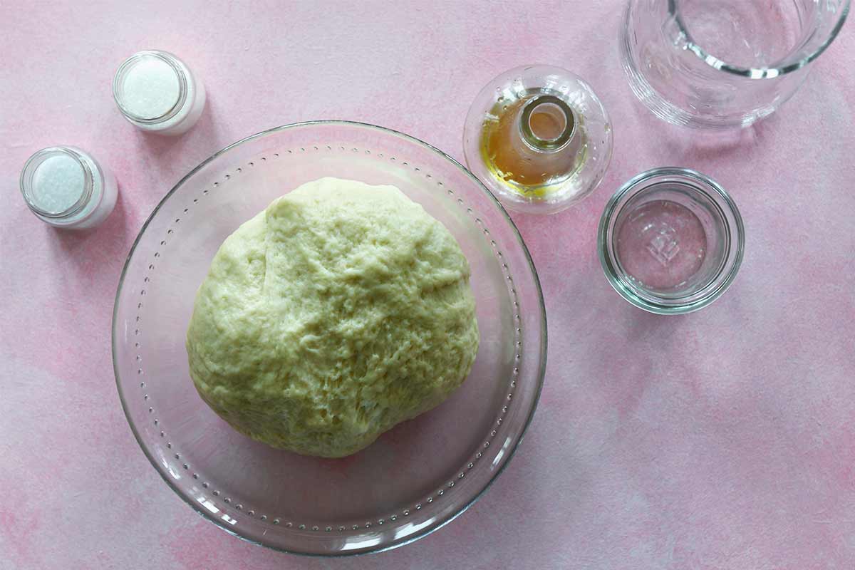 Eine Schüssel mit Hefeteig und den leeren Gefäsen für die Zutaten