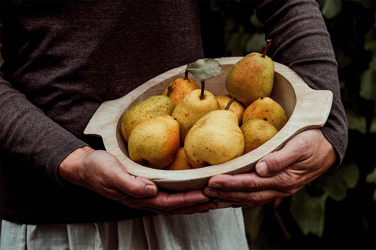 Eine Hand hält eine Holzschale mit Birnen