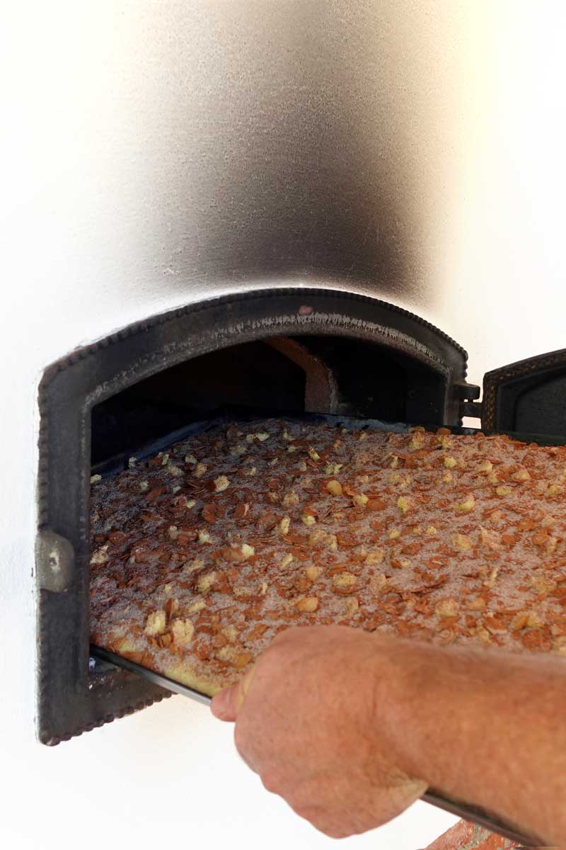 Eine Hand schiebt ein Stahlbackblech mit Butterkuchen in den Holzbackofen