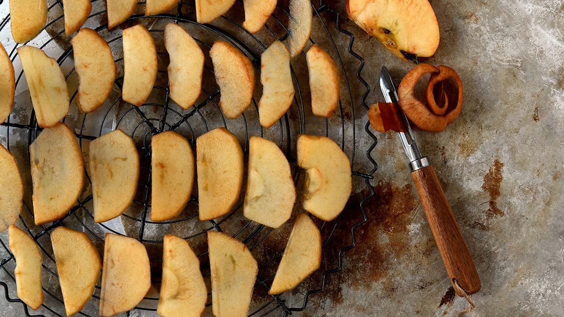 Frische Apfelscheiben nebeneinander auf Backblech mit Backpapier – bereit zum Trocknen im Ofen