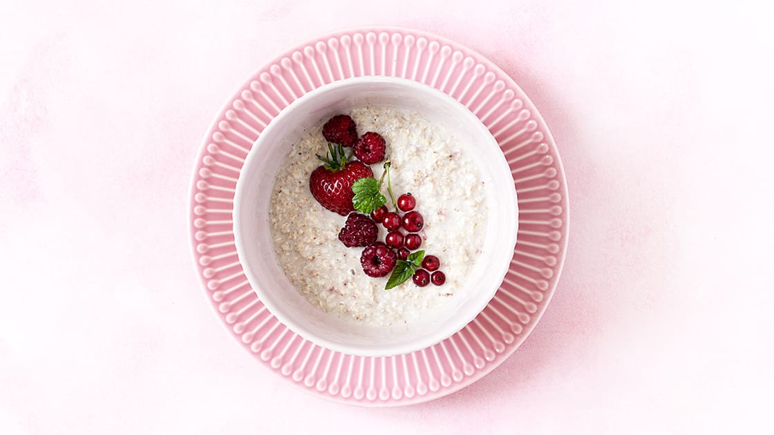 Selbst gemachtes Porridge mit roten Beeren in weißer Schüssel auf rosa Teller