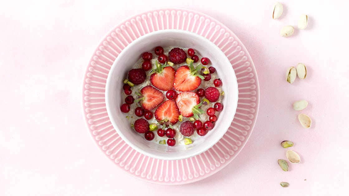 Porridge mit Erdbeeren, Johannisbeeren und Pistazien in weißer Schüssel