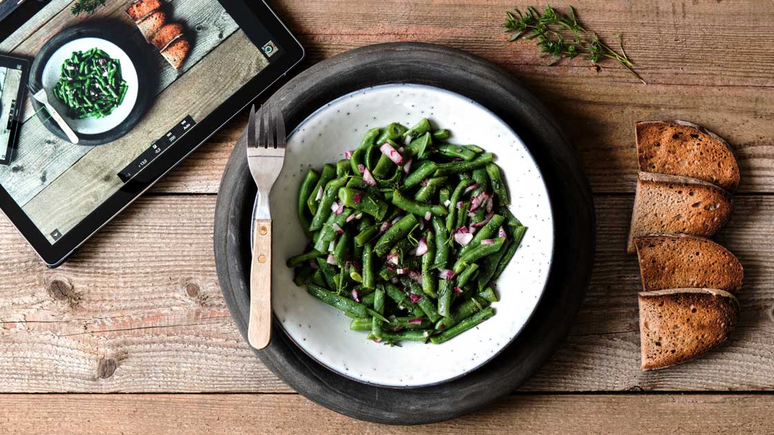 Einfacher Bohnensalat mit roten Zwiebeln und geröstetem Brot. Daneben ein Tablet, welches über Tethering das Aktuelle Bild der Kamera für Foodfotografie mit dem Tablet anzeigt