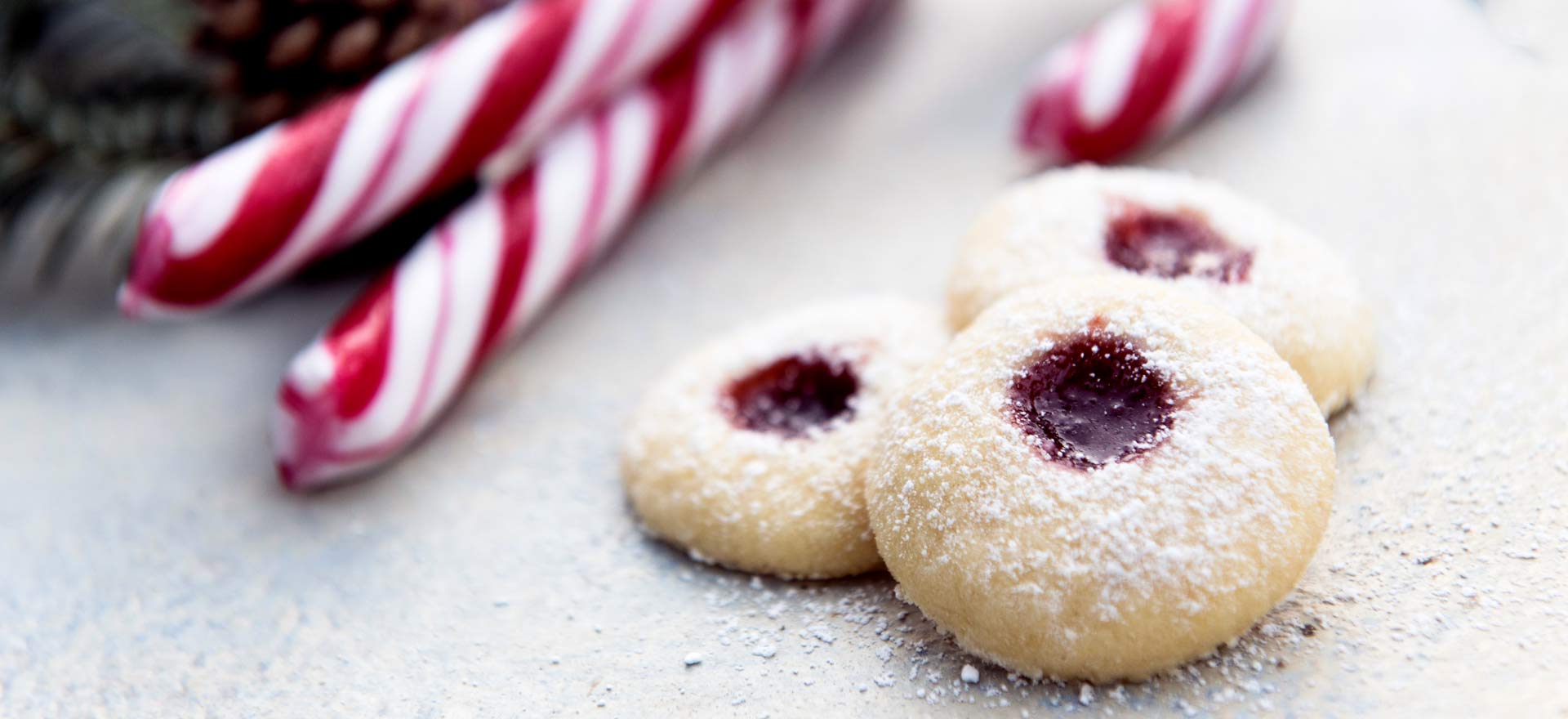 Foodfotografie Regensburg und Land: Weihnachtliches Gebäck - drei Engelsaugen. Im Hintergrund rot weiße Zuckerstangen