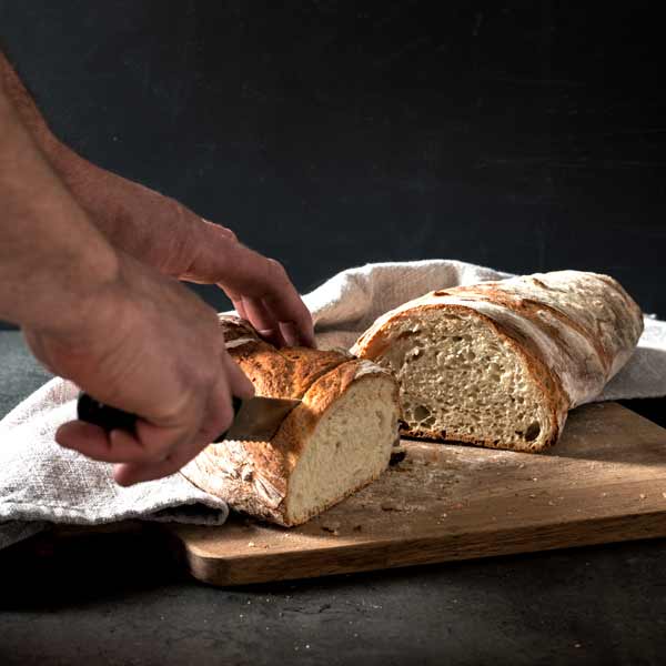 Hand schneidet Baguette - Weißbrot