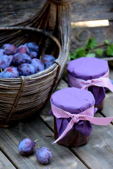 Ein Korb mit frisch geernteten Zwetschgen. Daneben zwei Gläser mit selbst gemachtem Zwetschgenmus dekoriert mit einem Tuch und einem bunten Band.